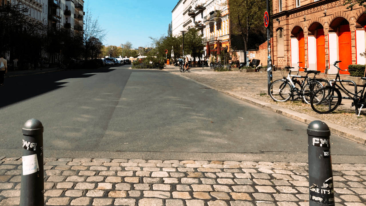 a street in berlin, in the foreground are a couple of bollards adorned with stickers